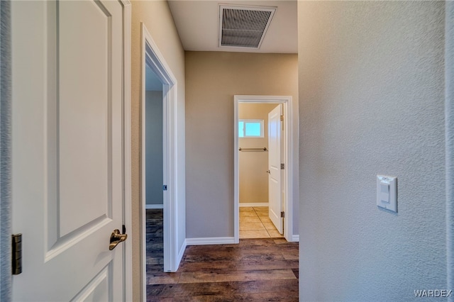 hall featuring a textured wall, dark wood-style flooring, visible vents, and baseboards