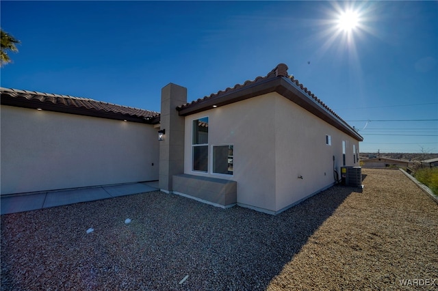 view of home's exterior with central AC, a patio area, a tiled roof, and stucco siding