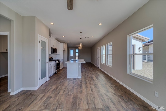 kitchen featuring stainless steel stove, light countertops, hanging light fixtures, white cabinetry, and an island with sink