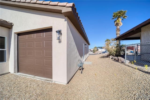 view of home's exterior with a garage, fence, a tile roof, and stucco siding