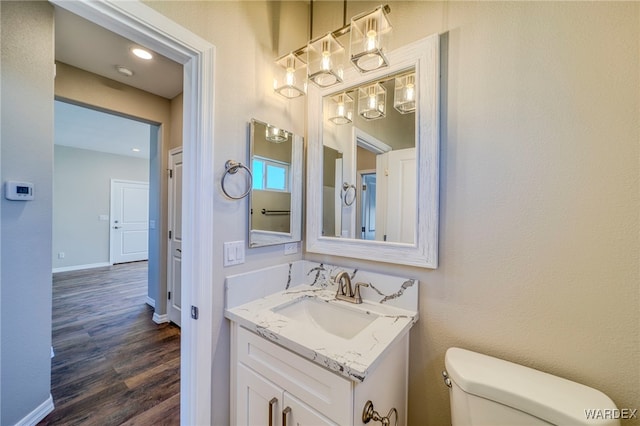 bathroom with toilet, baseboards, wood finished floors, and vanity