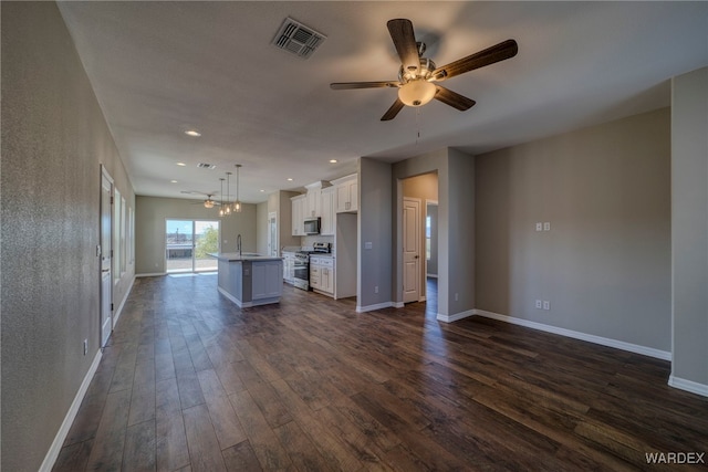 kitchen featuring stainless steel range with gas cooktop, decorative light fixtures, light countertops, open floor plan, and a kitchen island with sink