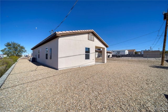 view of side of home featuring central air condition unit, a tile roof, fence, and stucco siding