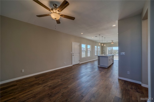 unfurnished living room with dark wood-type flooring, a sink, baseboards, and a ceiling fan