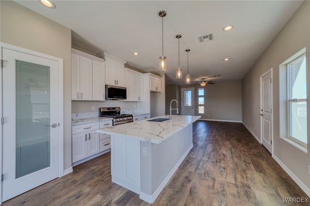 kitchen with light stone counters, stainless steel appliances, hanging light fixtures, white cabinetry, and an island with sink