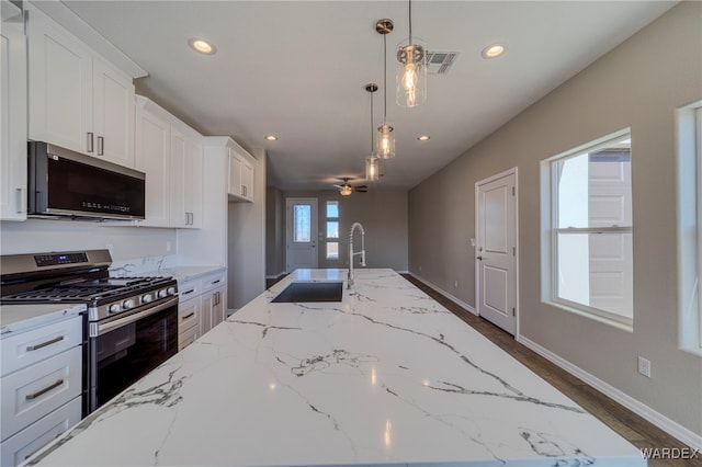 kitchen featuring white cabinets, light stone counters, stainless steel appliances, pendant lighting, and a sink