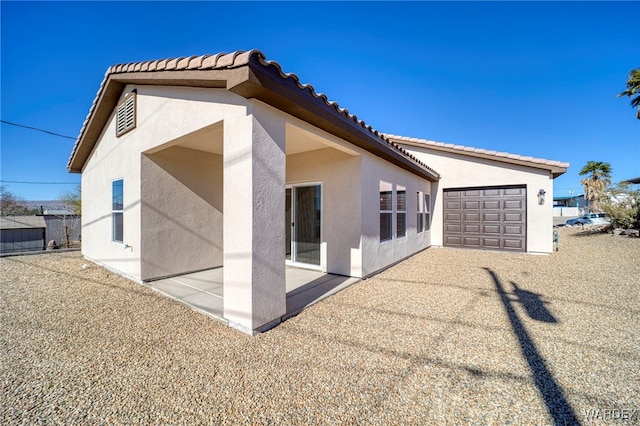 back of house with an attached garage, a patio area, a tile roof, and stucco siding