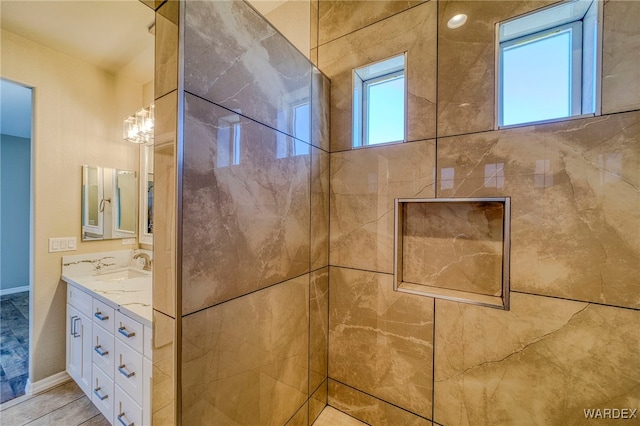 full bath featuring plenty of natural light, a tile shower, vanity, and baseboards