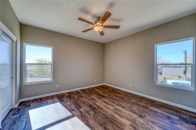 unfurnished room featuring dark wood-style flooring, a ceiling fan, and baseboards