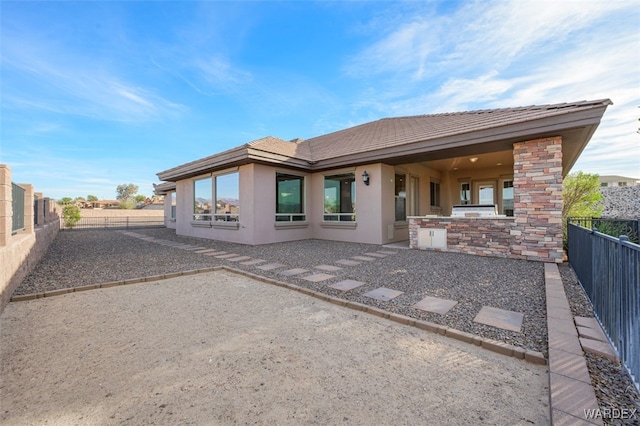 rear view of property with stone siding, a patio area, a fenced backyard, and stucco siding