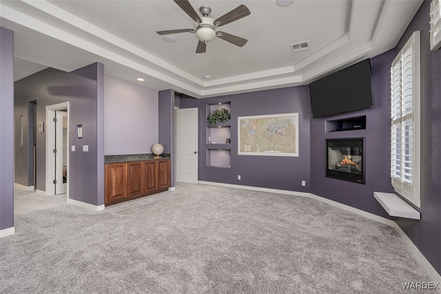 spare room with light carpet, baseboards, a raised ceiling, and a multi sided fireplace