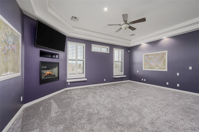 carpeted empty room with a glass covered fireplace, a raised ceiling, visible vents, and baseboards