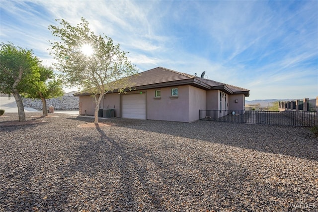 view of side of property with a garage, central AC unit, fence, and stucco siding