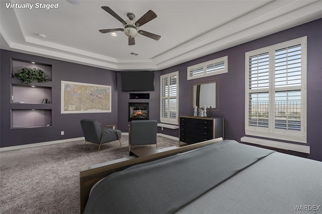 bedroom featuring visible vents, baseboards, a tray ceiling, carpet, and a glass covered fireplace