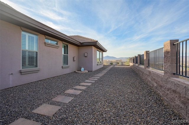 view of property exterior with a mountain view, a tile roof, fence, and stucco siding