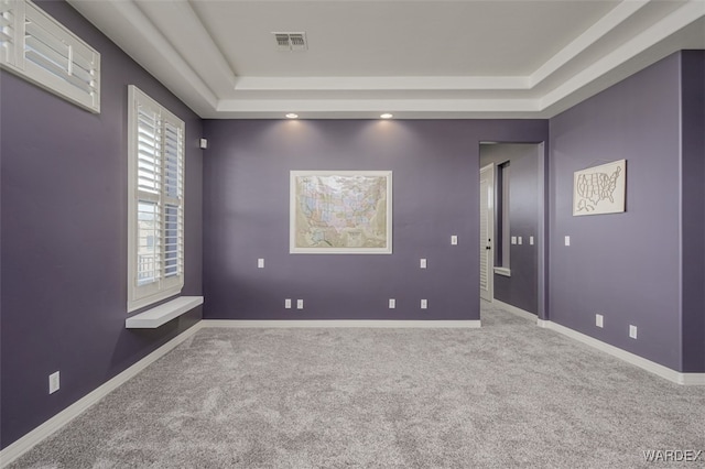 carpeted empty room featuring a raised ceiling, visible vents, and baseboards