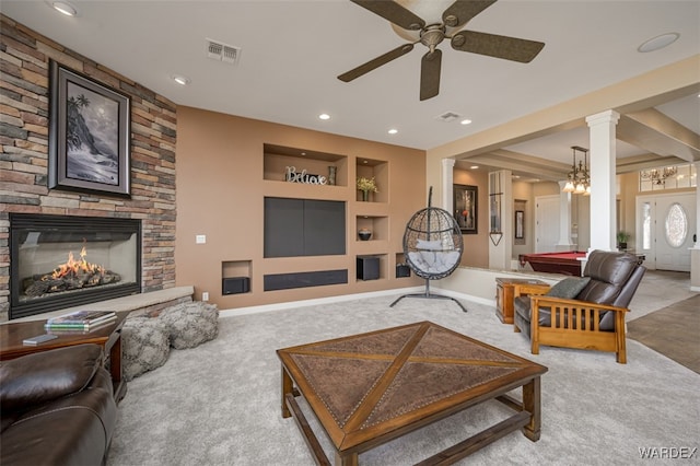 carpeted living room with baseboards, visible vents, a stone fireplace, ornate columns, and built in shelves