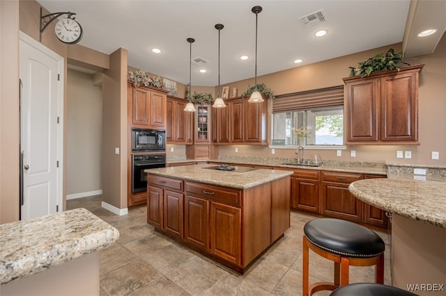 kitchen featuring visible vents, a kitchen island, glass insert cabinets, light stone counters, and black appliances