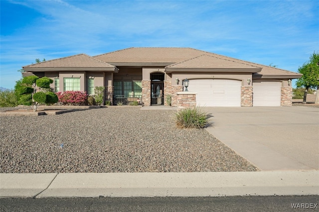 prairie-style house with a garage, stone siding, driveway, and stucco siding