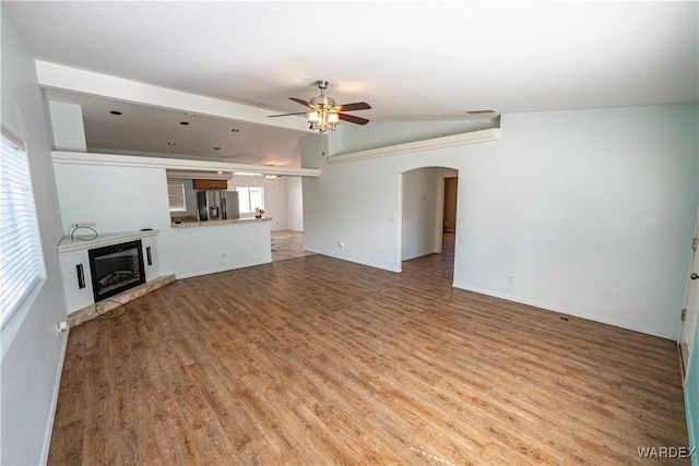 unfurnished living room with vaulted ceiling, wood finished floors, arched walkways, a glass covered fireplace, and a ceiling fan