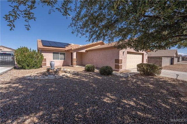 ranch-style house featuring stucco siding, roof mounted solar panels, fence, a garage, and a tiled roof