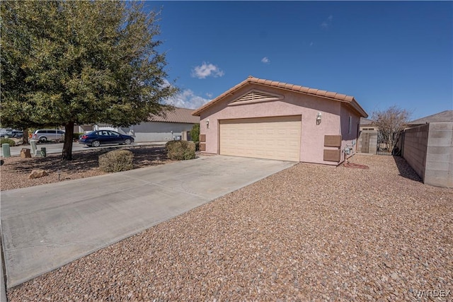 view of front of house featuring stucco siding, driveway, fence, an attached garage, and a tiled roof