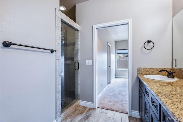 bathroom with a stall shower, baseboards, vanity, and wood finished floors