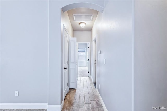 hallway with arched walkways, baseboards, visible vents, and light wood-style floors