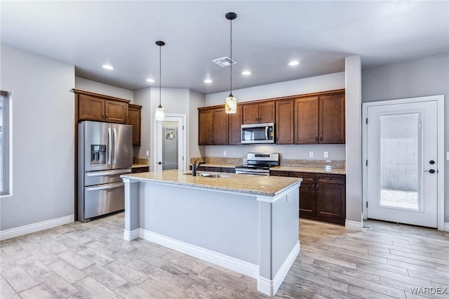 kitchen with a sink, light stone countertops, decorative light fixtures, appliances with stainless steel finishes, and recessed lighting