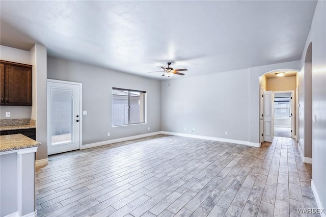 unfurnished living room with arched walkways, light wood-style floors, ceiling fan, and baseboards