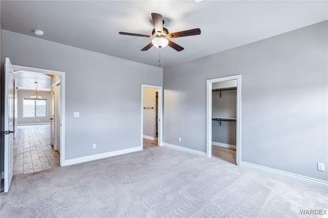 unfurnished bedroom featuring baseboards, ceiling fan with notable chandelier, carpet floors, and a walk in closet
