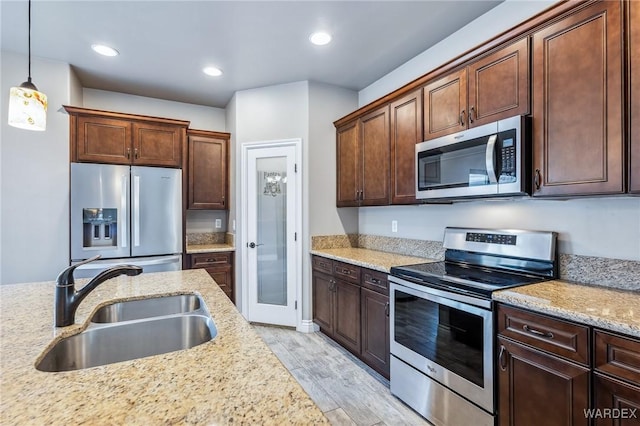 kitchen with light wood-style flooring, decorative light fixtures, light stone counters, a sink, and stainless steel appliances
