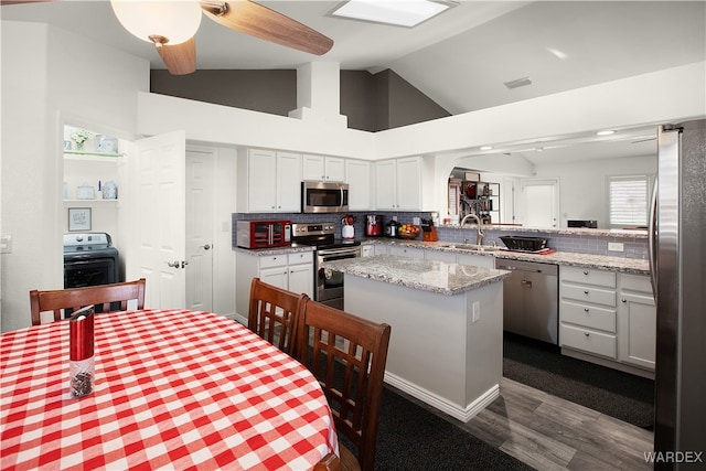 kitchen with light stone countertops, a peninsula, appliances with stainless steel finishes, a center island, and washer / dryer