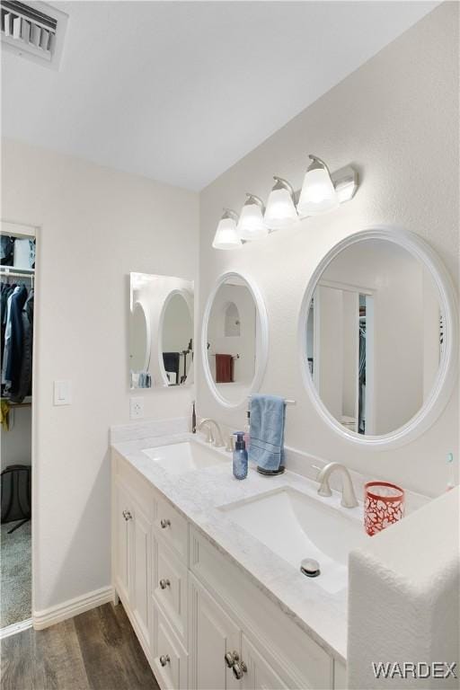 bathroom with double vanity, visible vents, a sink, and wood finished floors