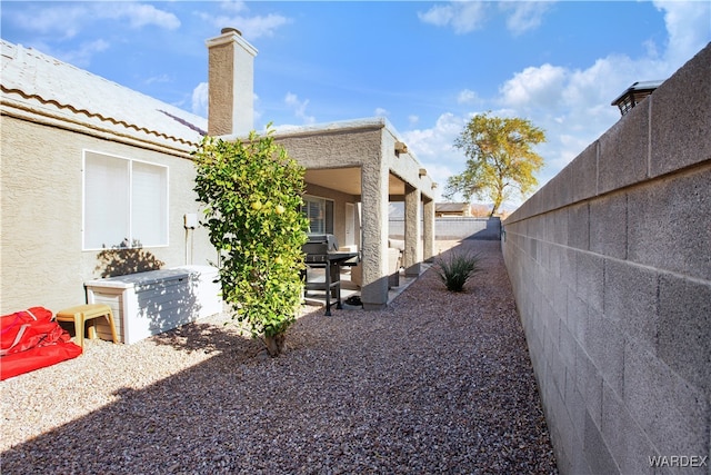 view of side of property featuring a patio, a fenced backyard, a tiled roof, and stucco siding