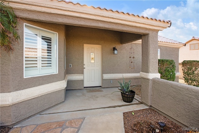 property entrance featuring a balcony, a tile roof, and stucco siding