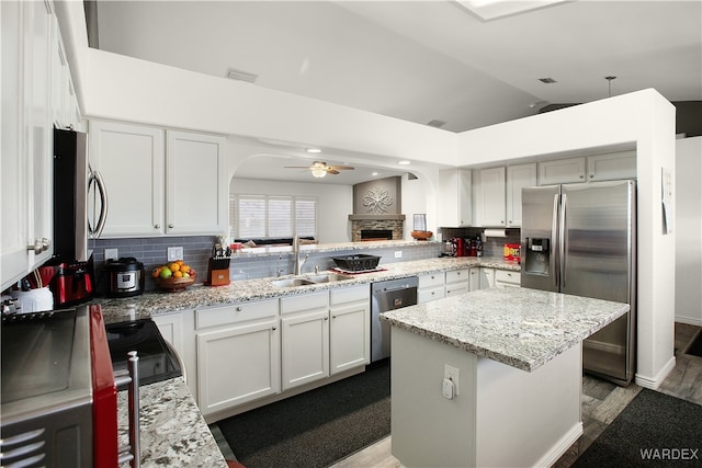 kitchen with appliances with stainless steel finishes, white cabinetry, a kitchen island, a sink, and light stone countertops