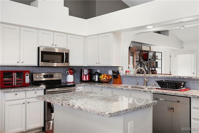 kitchen featuring decorative backsplash, appliances with stainless steel finishes, white cabinets, a sink, and light stone countertops