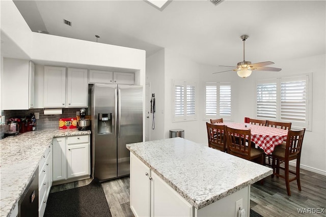 kitchen with light stone counters, backsplash, light wood-style floors, a kitchen island, and stainless steel fridge with ice dispenser