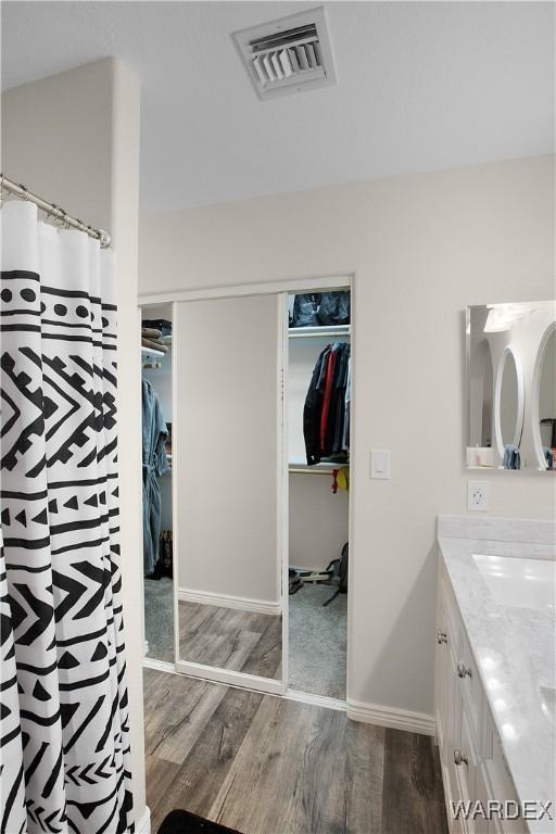 bathroom with vanity, wood finished floors, a walk in closet, and visible vents