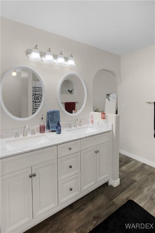 full bath with double vanity, wood finished floors, a sink, and baseboards