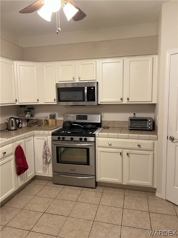 kitchen with tile countertops, appliances with stainless steel finishes, white cabinetry, and a ceiling fan