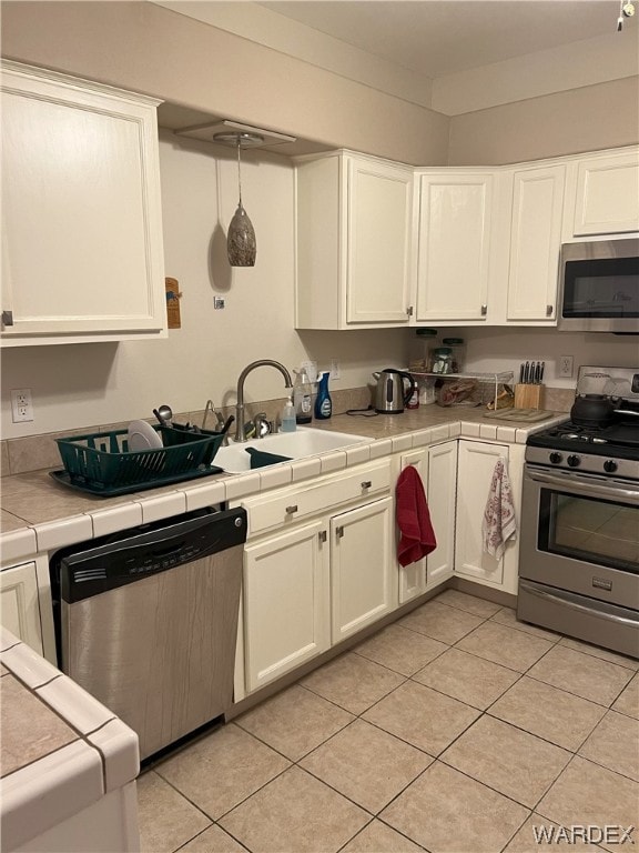 kitchen with stainless steel appliances, tile counters, white cabinets, and a sink