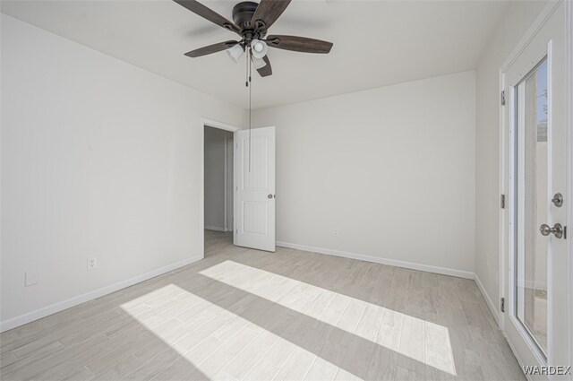 spare room featuring light wood finished floors, a ceiling fan, and baseboards