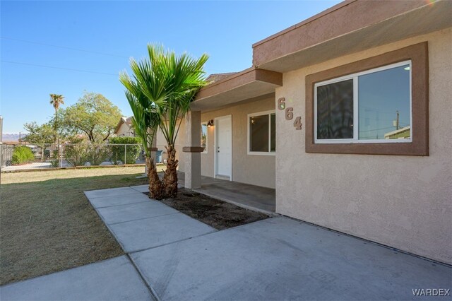 doorway to property with a yard, a patio, fence, and stucco siding