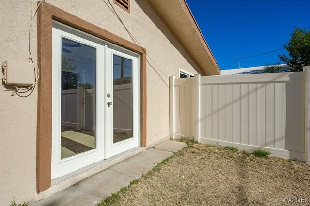 view of property exterior featuring stucco siding, fence, and french doors