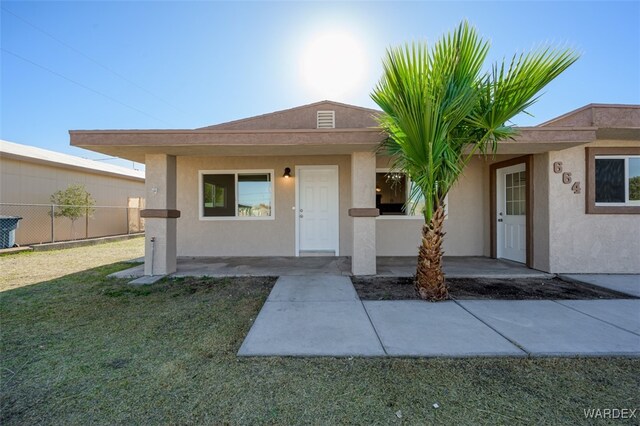 view of front of property with a patio area, fence, a front lawn, and stucco siding