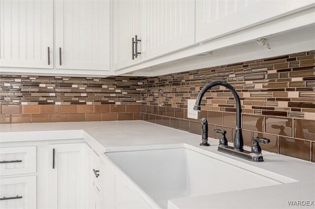 details with white cabinets, light countertops, a sink, and backsplash