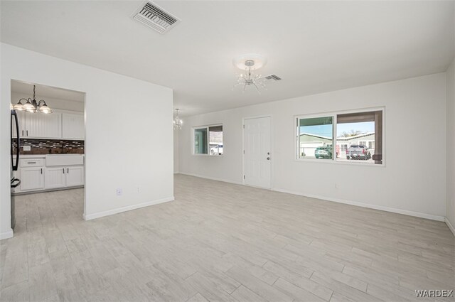 unfurnished living room featuring light wood finished floors, baseboards, visible vents, and a notable chandelier