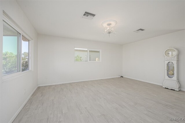 unfurnished room with a chandelier, light wood finished floors, and visible vents